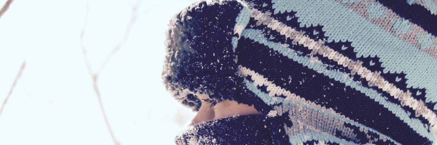 close up of child wearing scarf and tuque staring through fence in winter