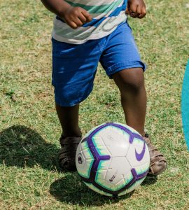 small child kicking soccer ball on grass